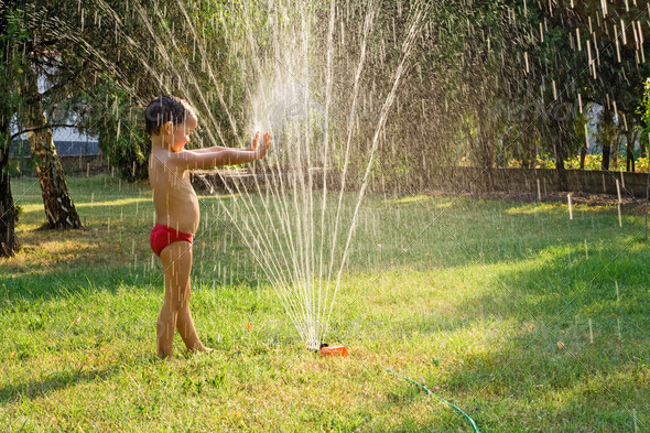 Young boy having fun playing with water from a sprinkler in the garden