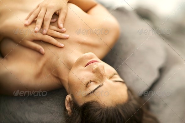 Close up of young nude Caucasian woman lying on rock with eyes closed and hands crossed on chest.