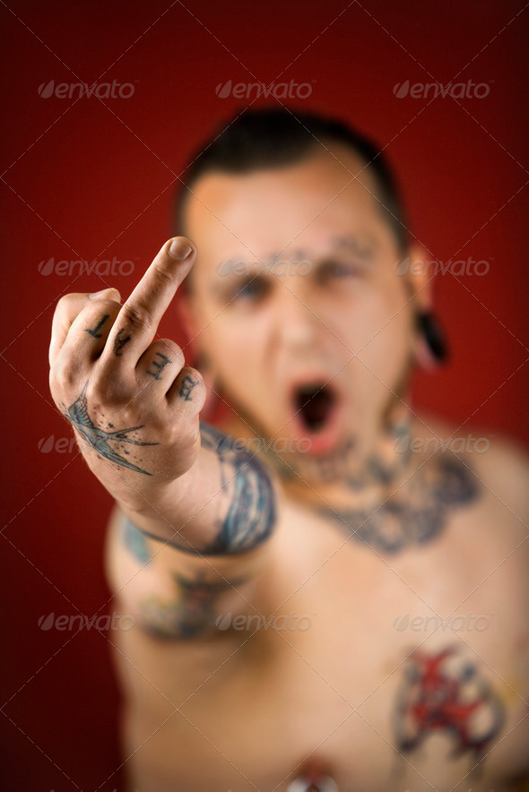 Caucasian midadult man with tattoos and piercings holding up middle finger
