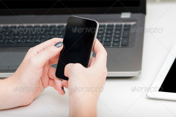 Touching, using smart, mobile phone. Computer and touch pad-tablet in the background. Telephone in hands.
