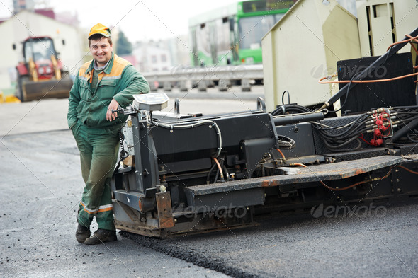 happy road construction worker near asphalt paver machine