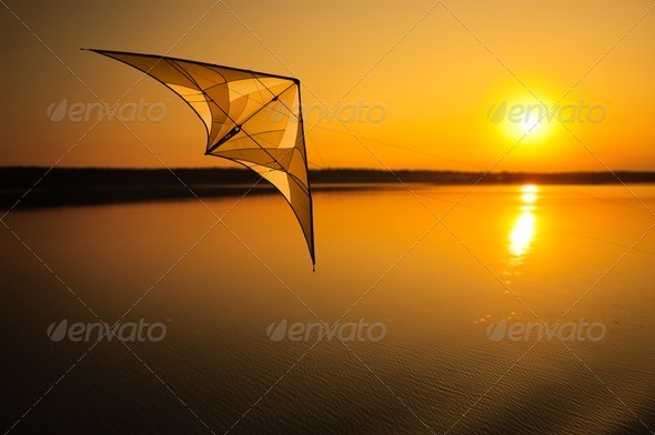 Kite flying over peaceful lake at sunset