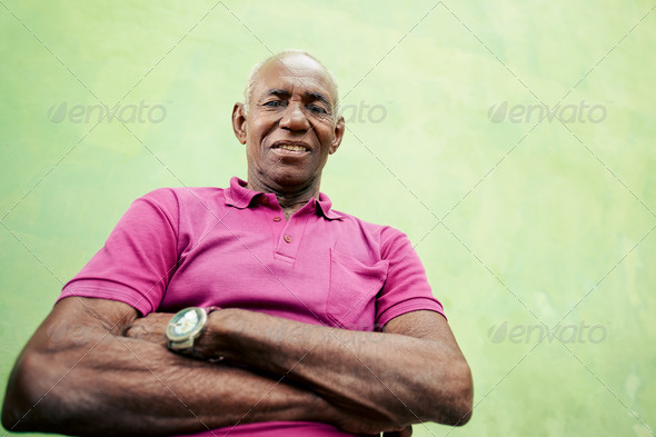 Old people and emotions, portrait of senior african american man looking and smiling at camera with arms crossed. Copy space, low angle view,