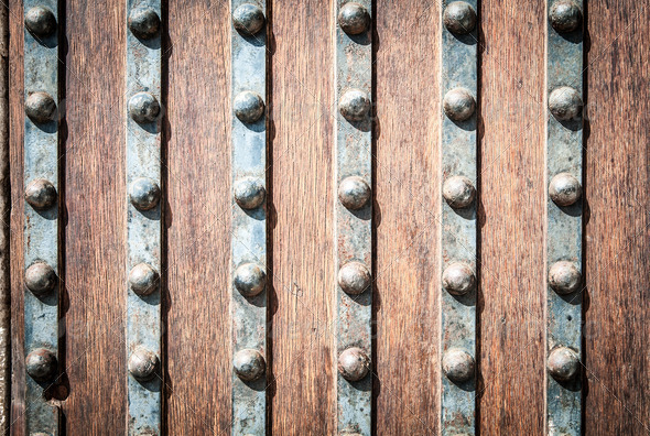 Detail of old solid door. Striped wood and metal door with metallic rivets looking worn and grungy. Part of ancient castle or fortress. Abstract backgrounds and wallpapers.