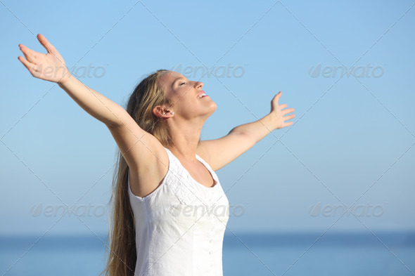 Attractive blonde woman breathing happy with raised arms with the sea in the background