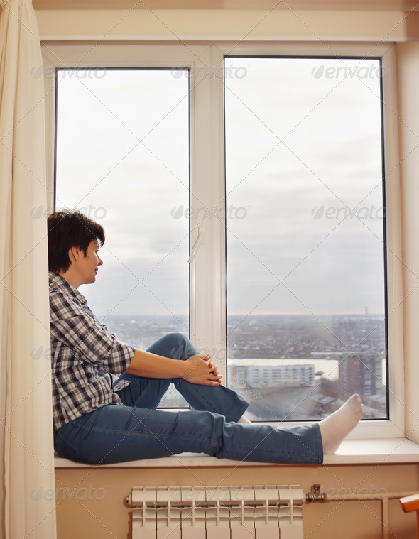Middle aged pretty woman sitting on the windowsill