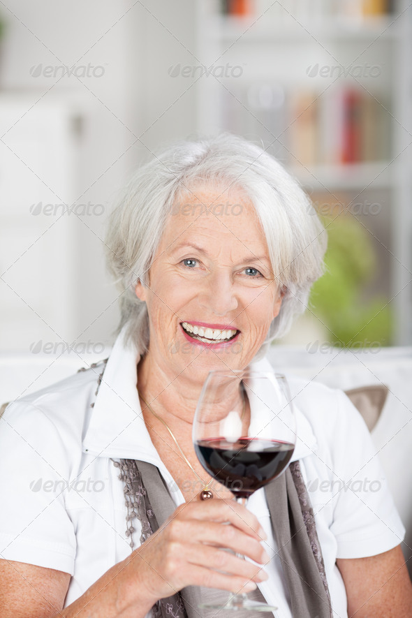 Senior woman enjoying a glass of wine raising her wineglass in a toast as she gives the camera a beautiful smile