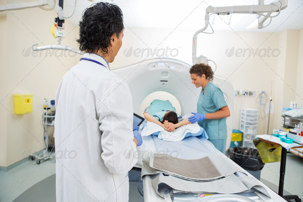 Doctor Looking At Nurse Preparing Patient For CT Scan