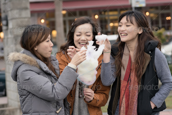 Happy young Asian woman eating cotton candy with her friends