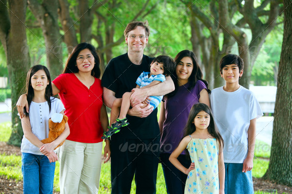 Large multiracial family of seven. Father is holding disabled son with cerebral palsy.