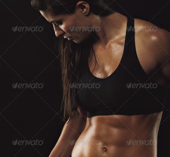 Image of fitness woman in sports clothing working out on black background. Young female with perfect muscular body.