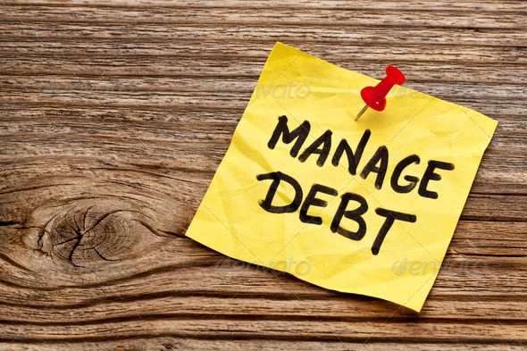 manage debt – yellow reminder note against grained wood board