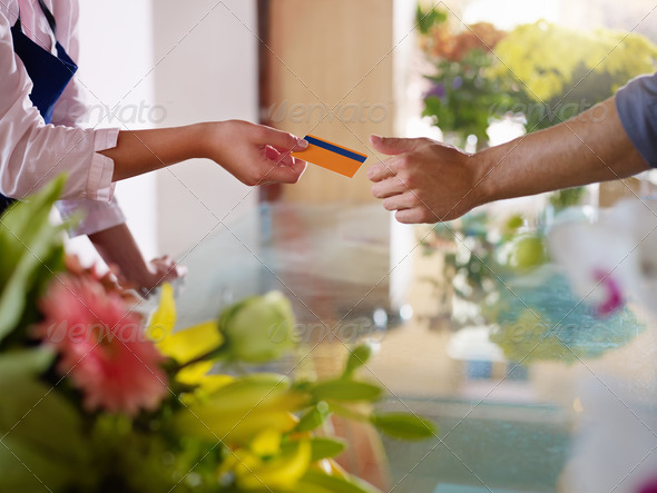 Young woman working as florist giving credit card to customer after purchase. Horizontal shape, closeup