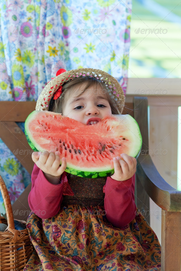 little girl in a straw hat with appetite eats a ripe water-melon